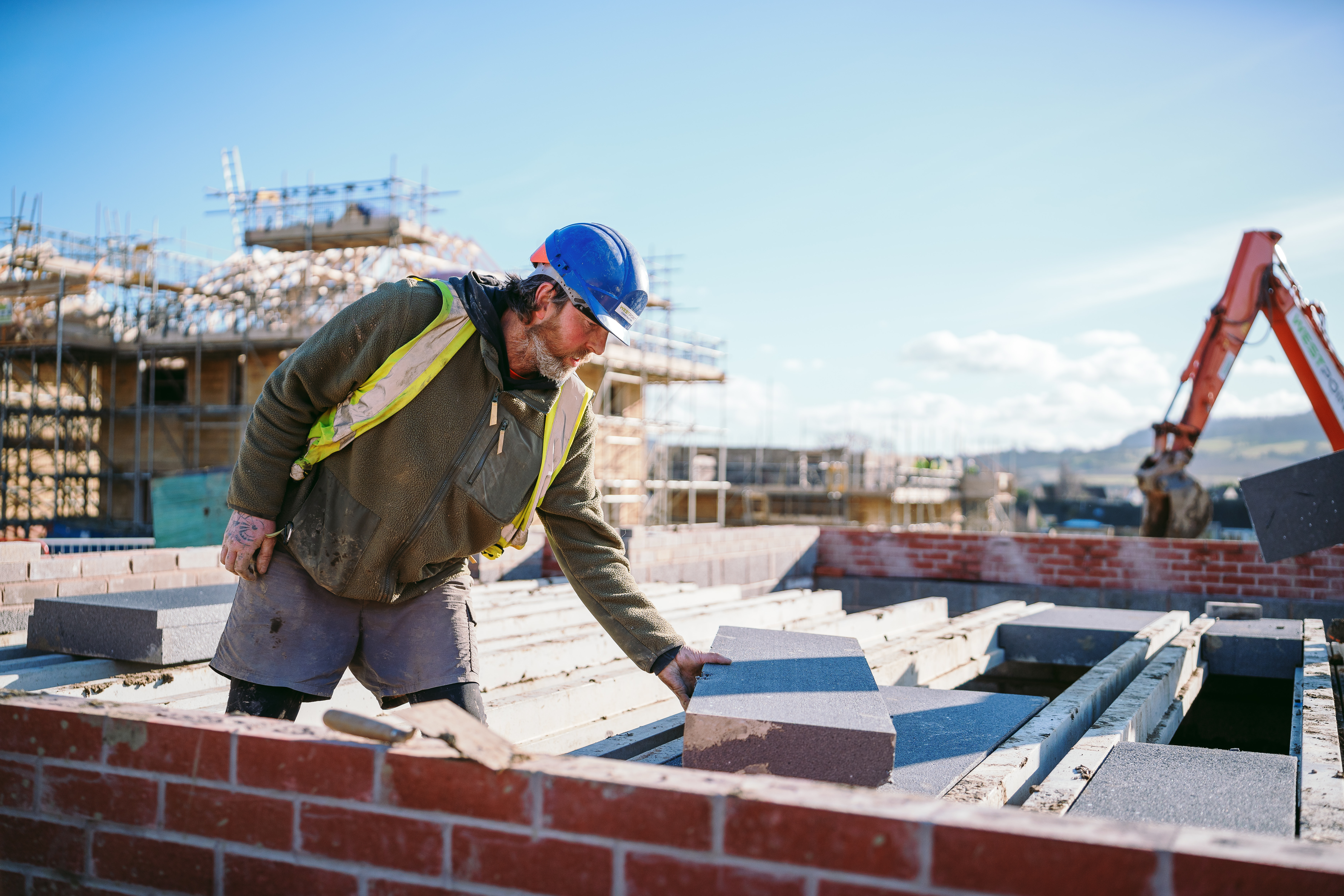 A construction worker in high-vis and a hard hat on a construction site next to a part-built brick wall.