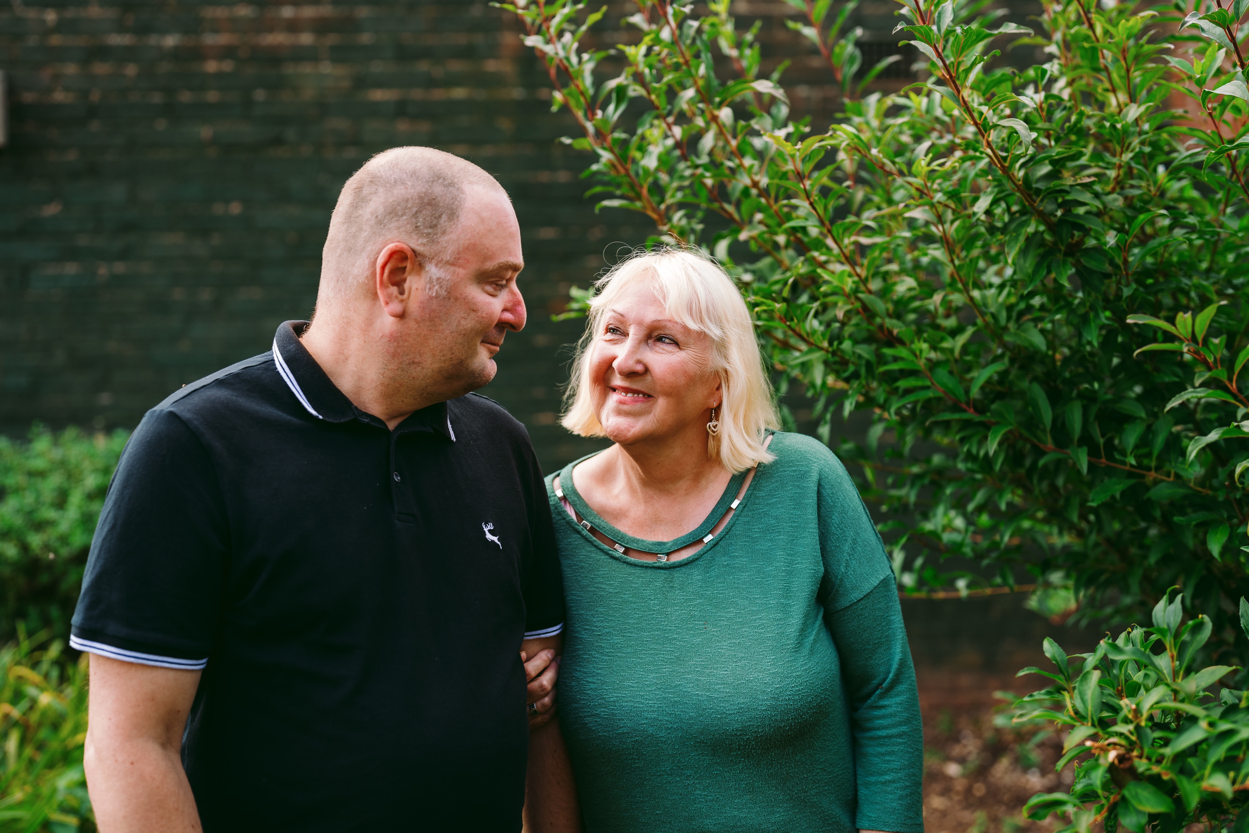 A man (left) and a woman look at each other, standing in a garden
